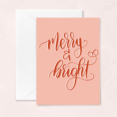 pink christmas greeting card with red handlettered script that says merry and bright