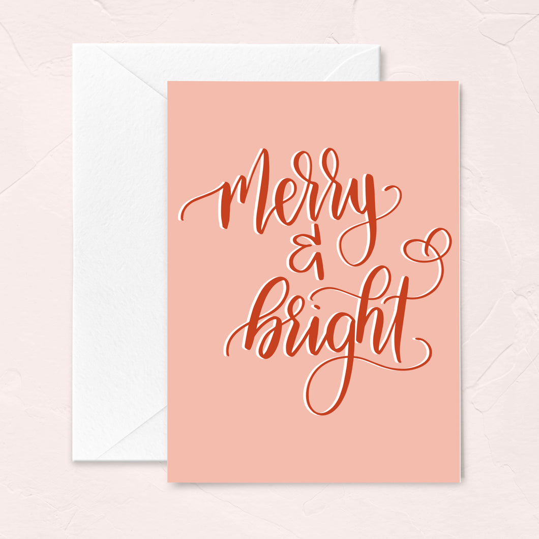 pink christmas greeting card with red handlettered script that says merry and bright